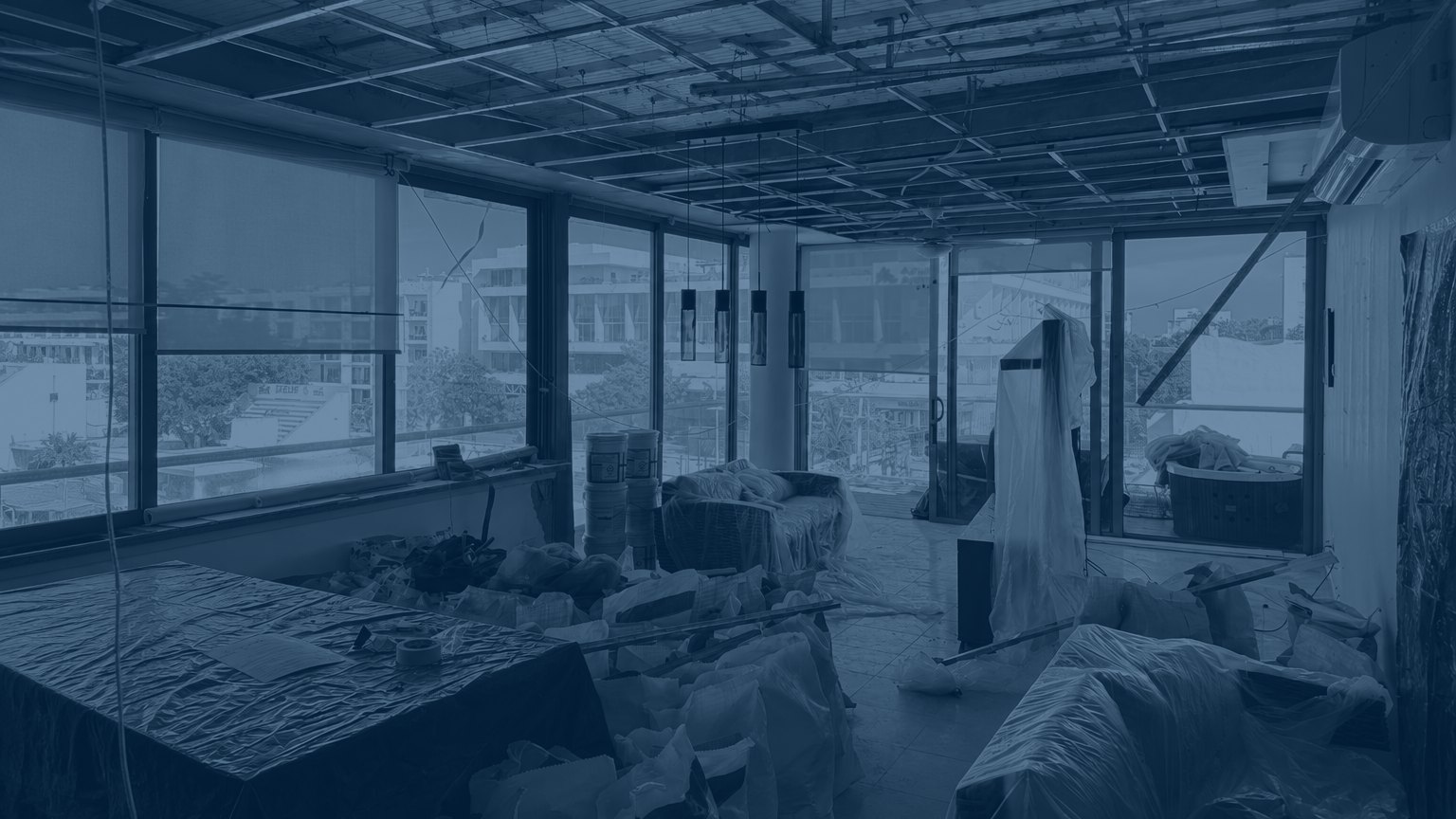 Apartment under renovation at DOCA 303: ceiling stripped to the metal framing, furniture covered and materials staged, with the sea visible beyond